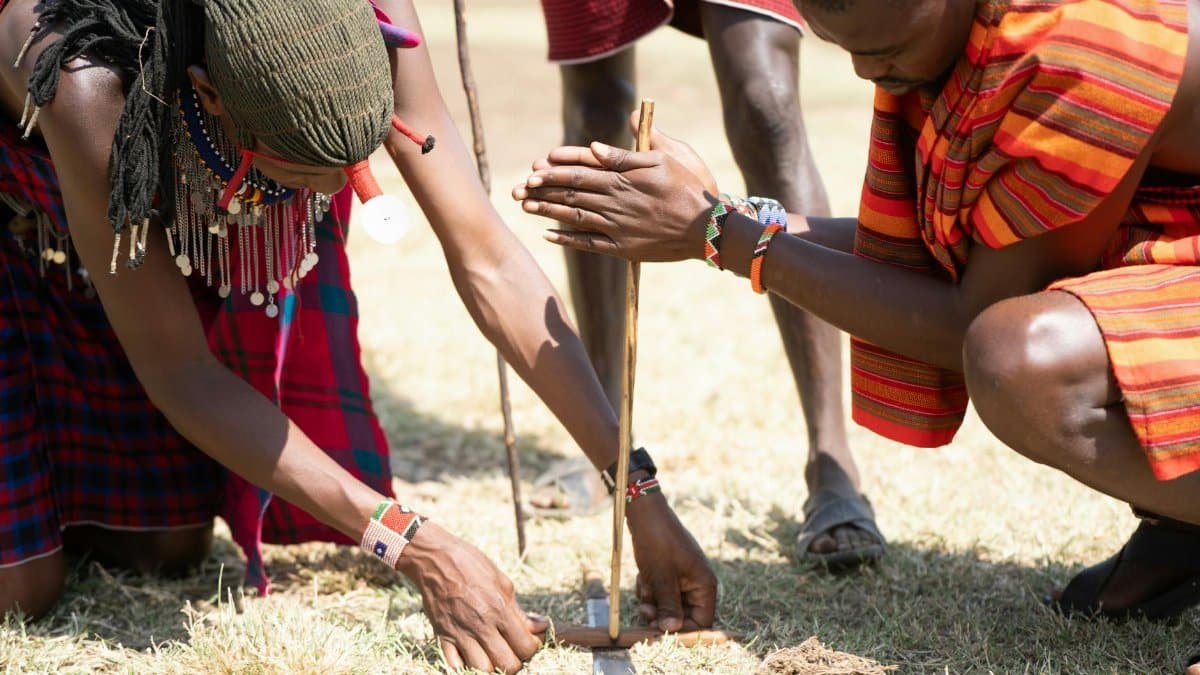Masai tribe members in Kenya demonstrate traditional fire-making techniques outdoors.