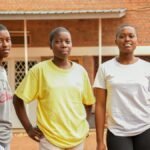 Three young women outdoors in Southern Province, Rwanda, standing in a courtyard.