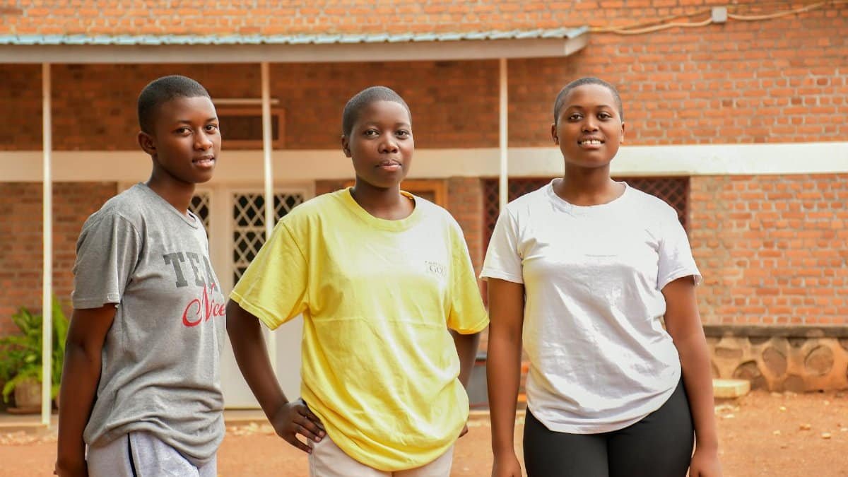 Three young women outdoors in Southern Province, Rwanda, standing in a courtyard.