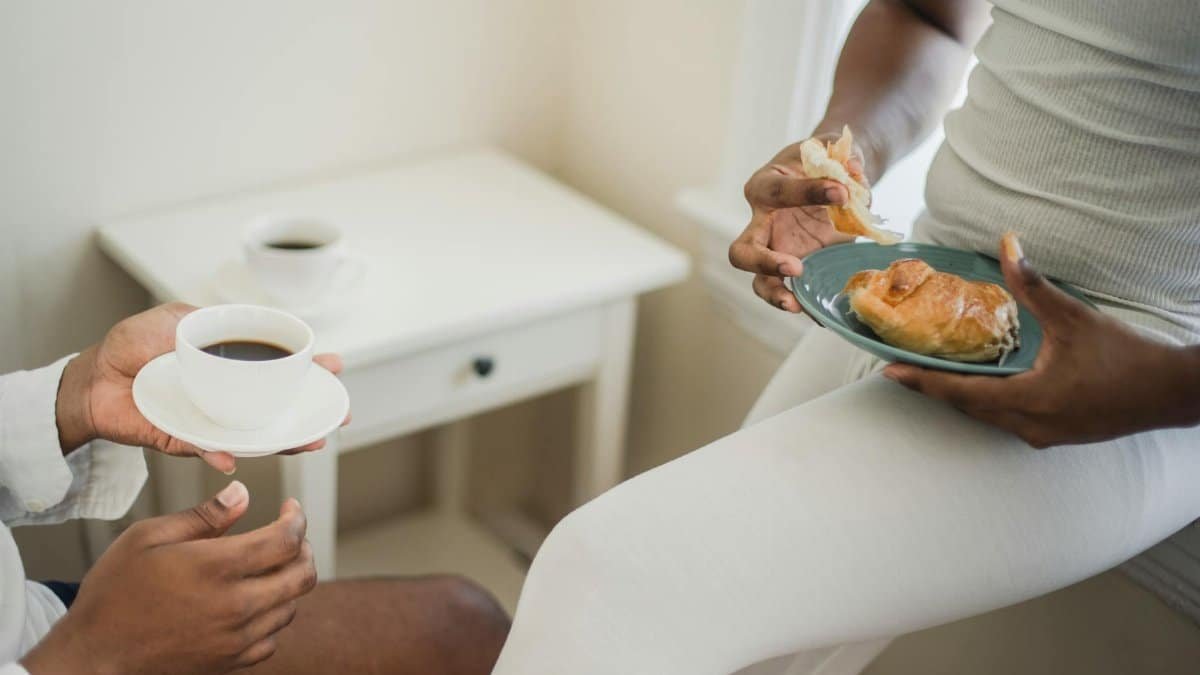 Two people enjoying coffee and a pastry indoors, creating a cozy breakfast atmosphere.