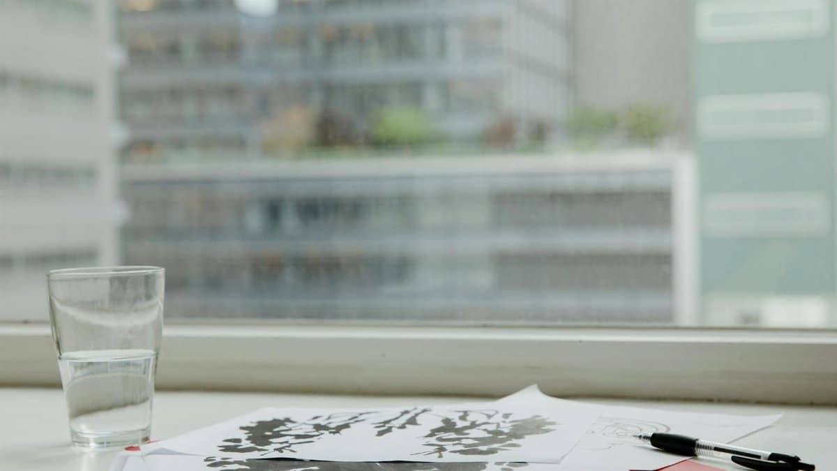 A minimalist office desk setup featuring psychological test papers, a glass of water, and a pen.