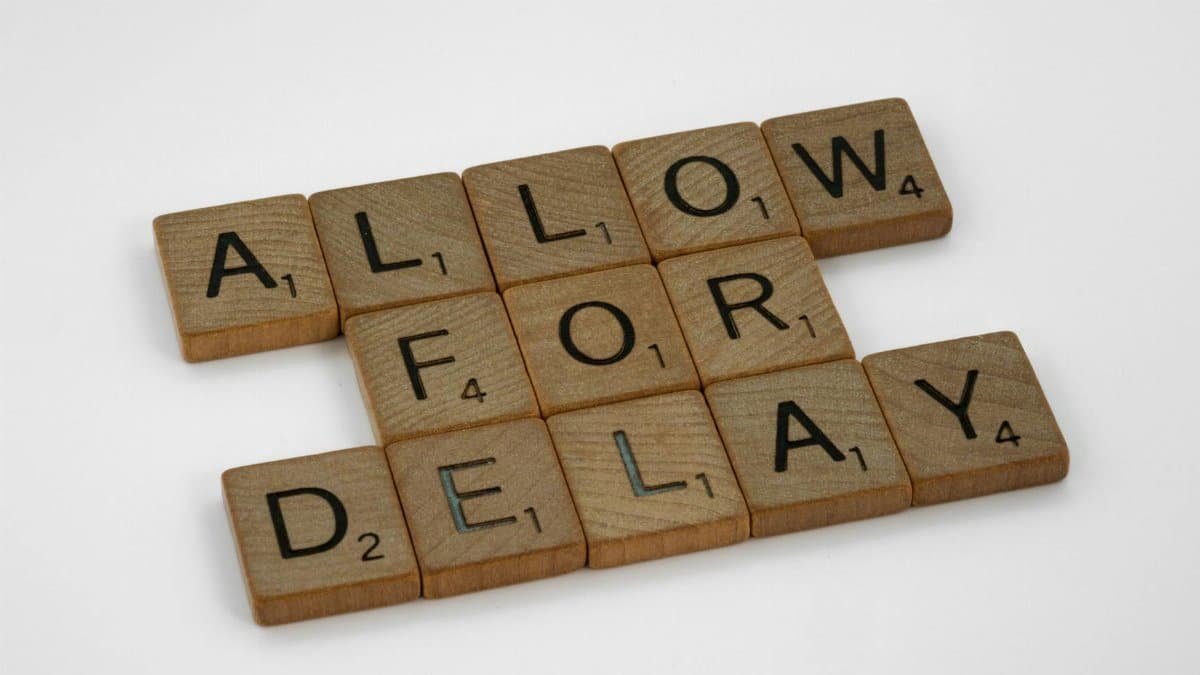 Wooden letter tiles on a white background spelling 'Allow for Delay'.