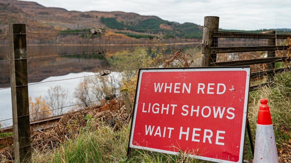 Red traffic sign by a scenic roadside urging drivers to wait. Autumn landscape reflected in water.