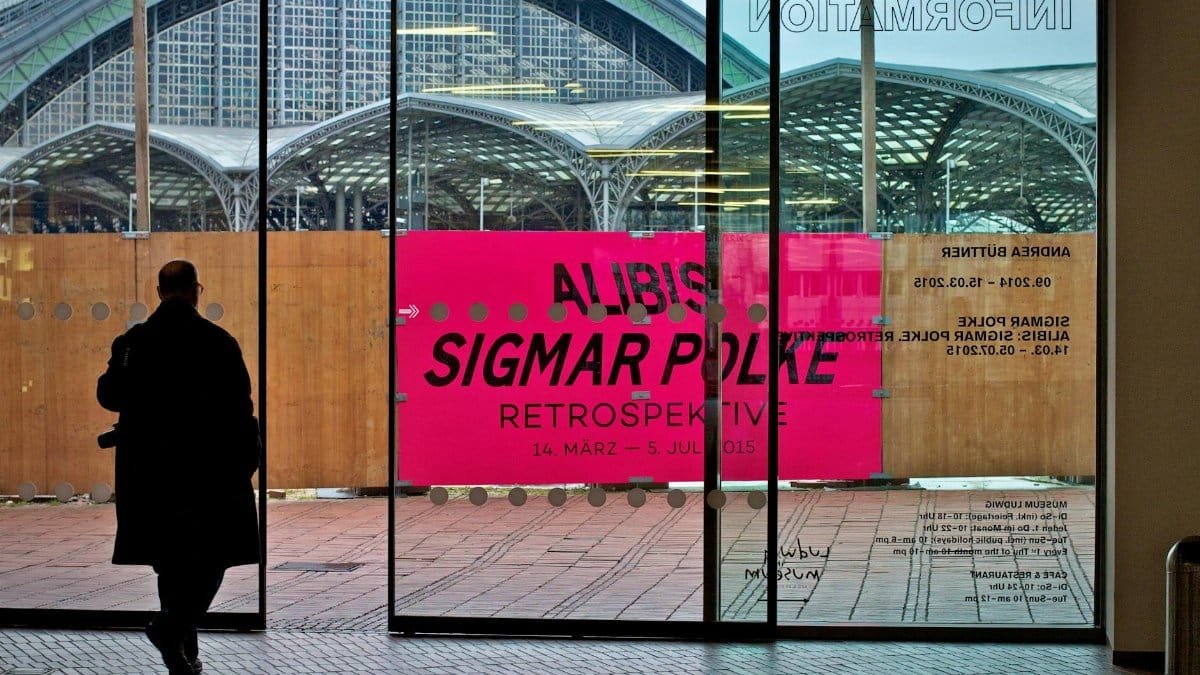 A silhouette of a man walking past an art exhibition poster at a gallery entrance.