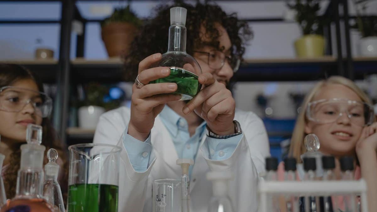 Students working on a chemistry experiment with flasks and colored liquids in a classroom setting.
