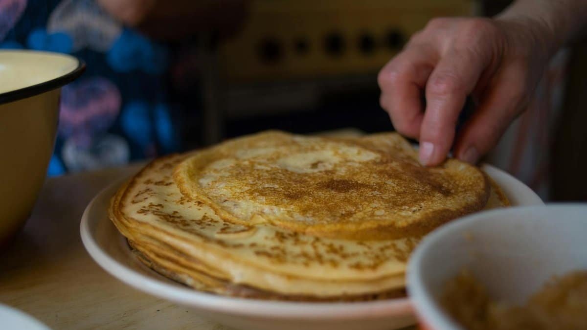 A stack of homemade pancakes being touched by a hand in a cozy kitchen setting.