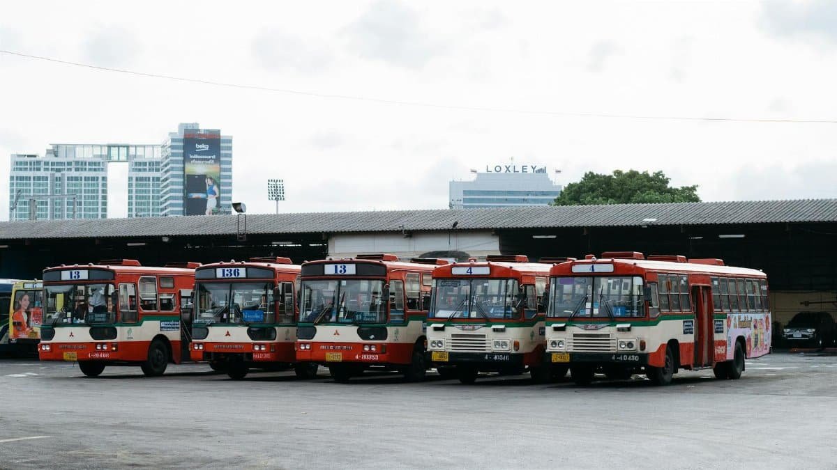 Five public buses lined up at a bus terminal in Bangkok, Thailand.