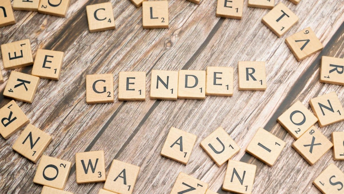 Wooden letter tiles spelling 'gender' on a wooden background, depicting identity and expression.