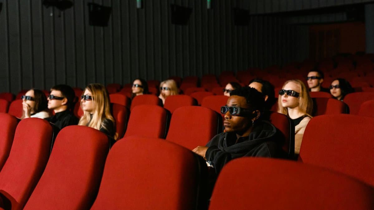 Diverse audience wearing 3D glasses in cinema with red seats, watching a film.