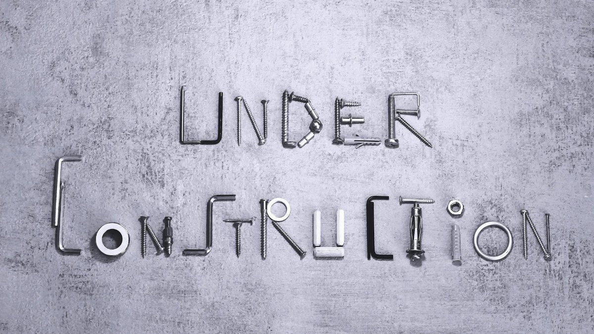 Under construction text creatively formed using various screws and tools on a concrete background.
