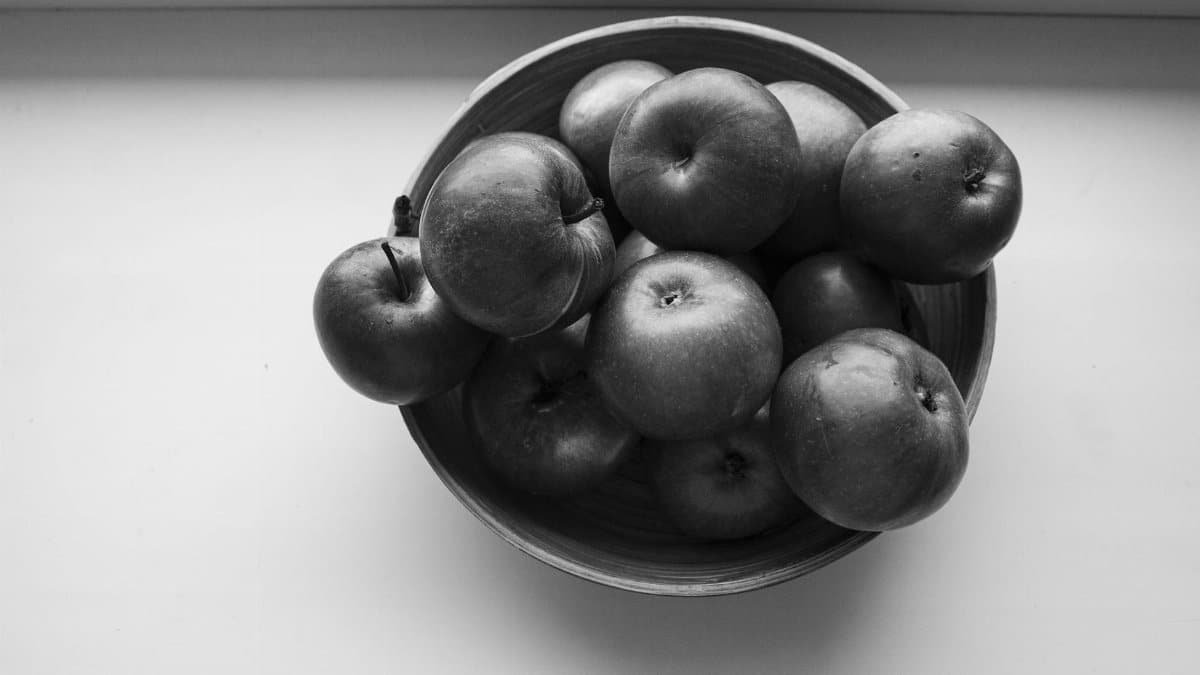 Monochrome image of a bowl filled with fresh apples on a wooden surface.