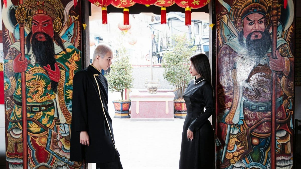Couple in traditional attire at a colorful Asian temple entrance with guardian paintings.