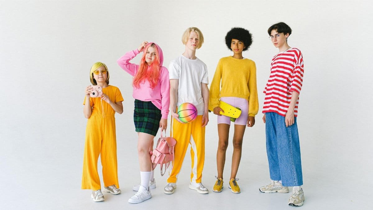 A vibrant group of teenagers in colorful outfits posing with various accessories in a studio setting.