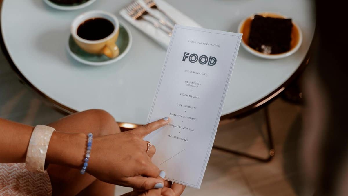 Hands holding a menu, selecting options at a cozy cafe with coffee and dessert on the table.