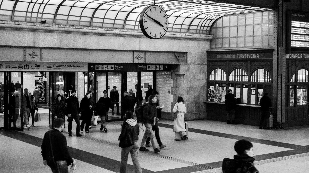 Monochrome view of a crowded train station with a prominent clock and ticket counters.