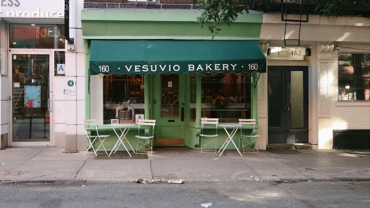 Street view of Vesuvio Bakery with green awning and outdoor seating. Iconic urban charm.