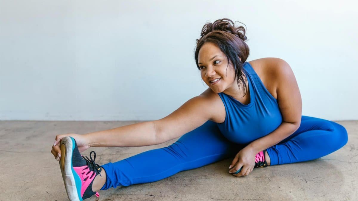 A plus-size woman in blue activewear stretching indoors, promoting body positivity and wellness.