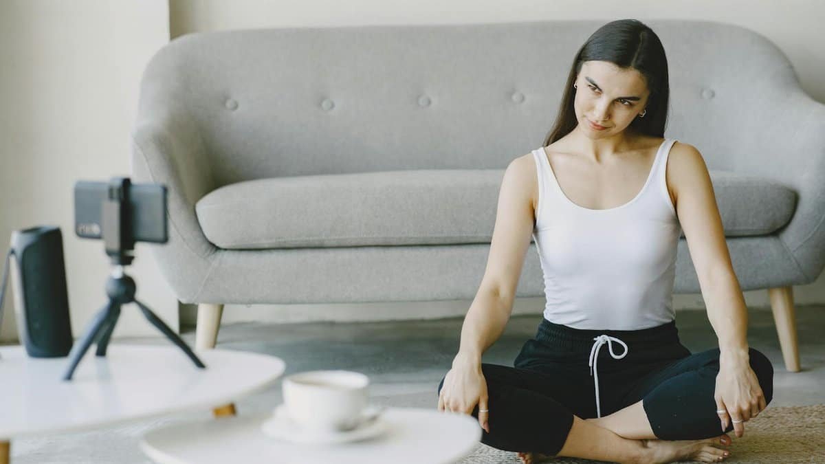 A woman in workout attire doing yoga at home, recording on a smartphone.
