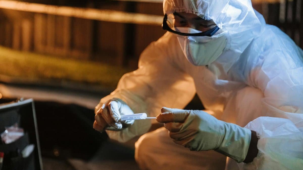 A forensic investigator in protective gear collects evidence outdoors at night.