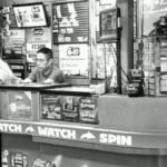 A man reads at a busy lottery ticket booth filled with signs and advertisements.