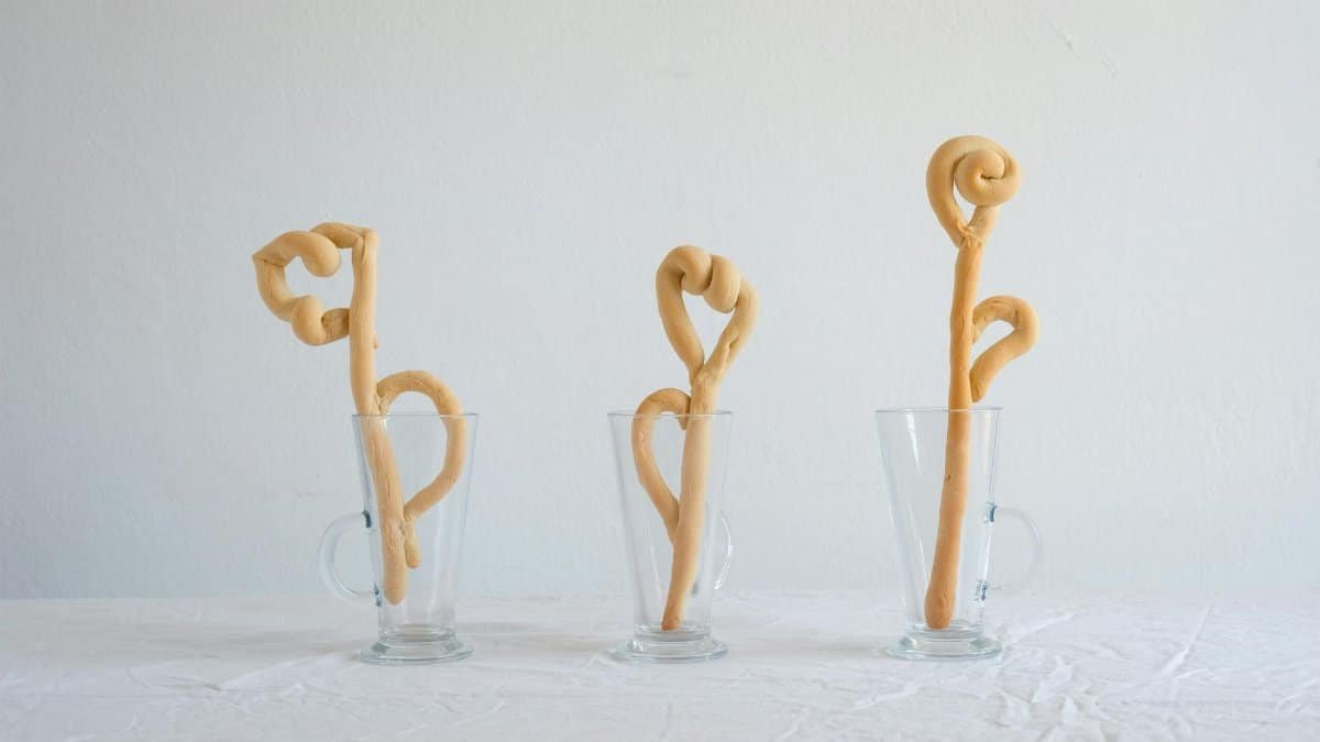Creative display of artfully twisted dough arranged in glass mugs on a tablecloth.