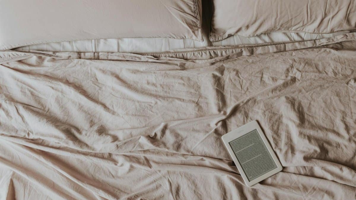 A Kindle e-reader on a neatly arranged bed with beige sheets. Perfect for relaxation and reading.