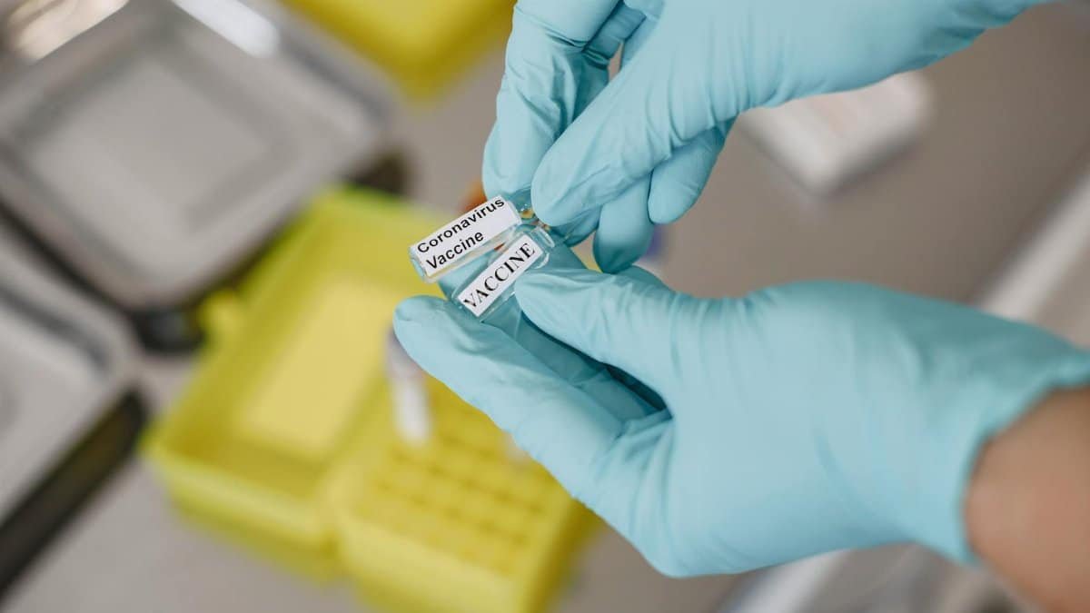 Gloved hands holding a labeled coronavirus vaccine vial, representing healthcare and laboratory research.