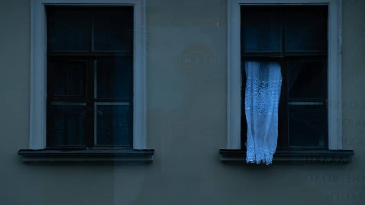 Dark facade with vintage windows and lace curtains at twilight, evoking calmness.