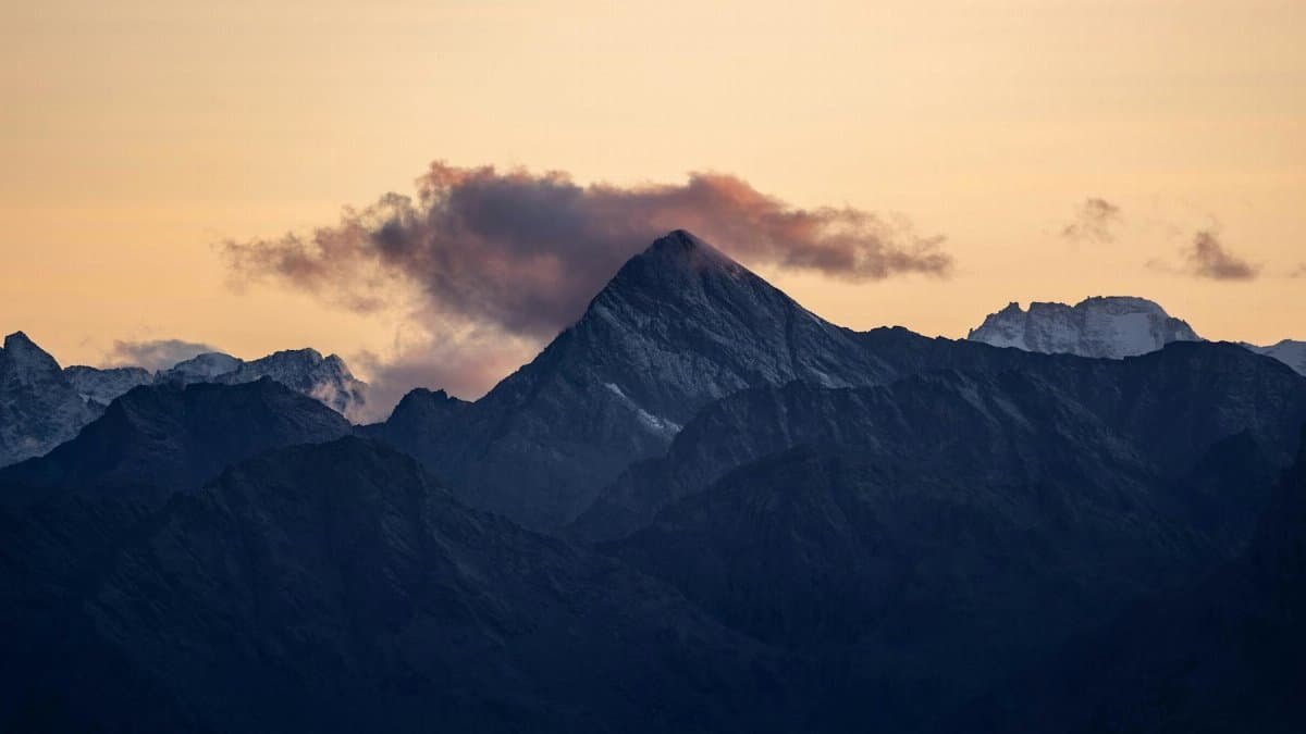 Breathtaking view of a mountain peak in the Alps during sunset with colorful clouds.