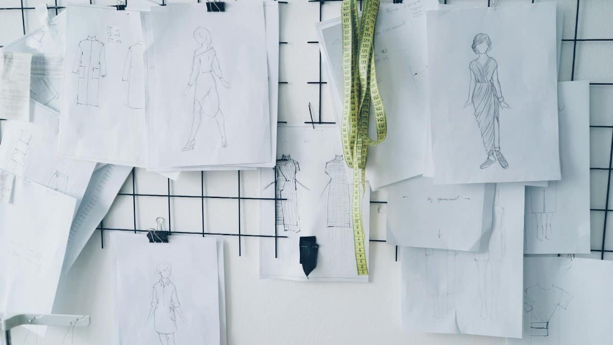 Fashion sketches and measuring tape hang on a designer's workspace wall.