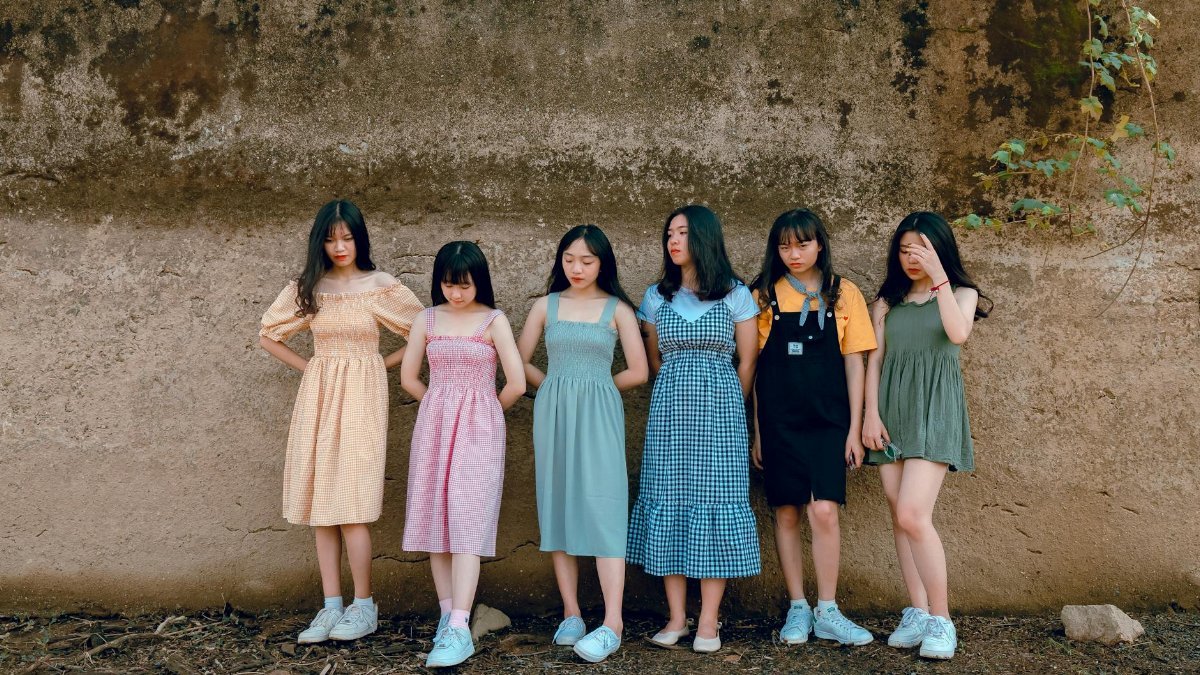 Group of young women in vibrant summer dresses posing against a rustic wall outdoors.