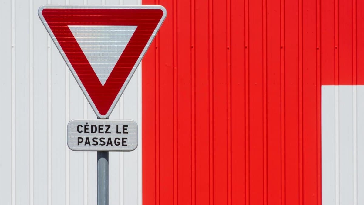 A French yield sign 'Cédez le passage' stands against a vivid red wall.