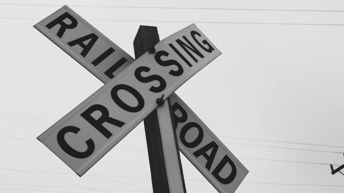 Black and white photo of a railroad crossing sign against a clear sky.