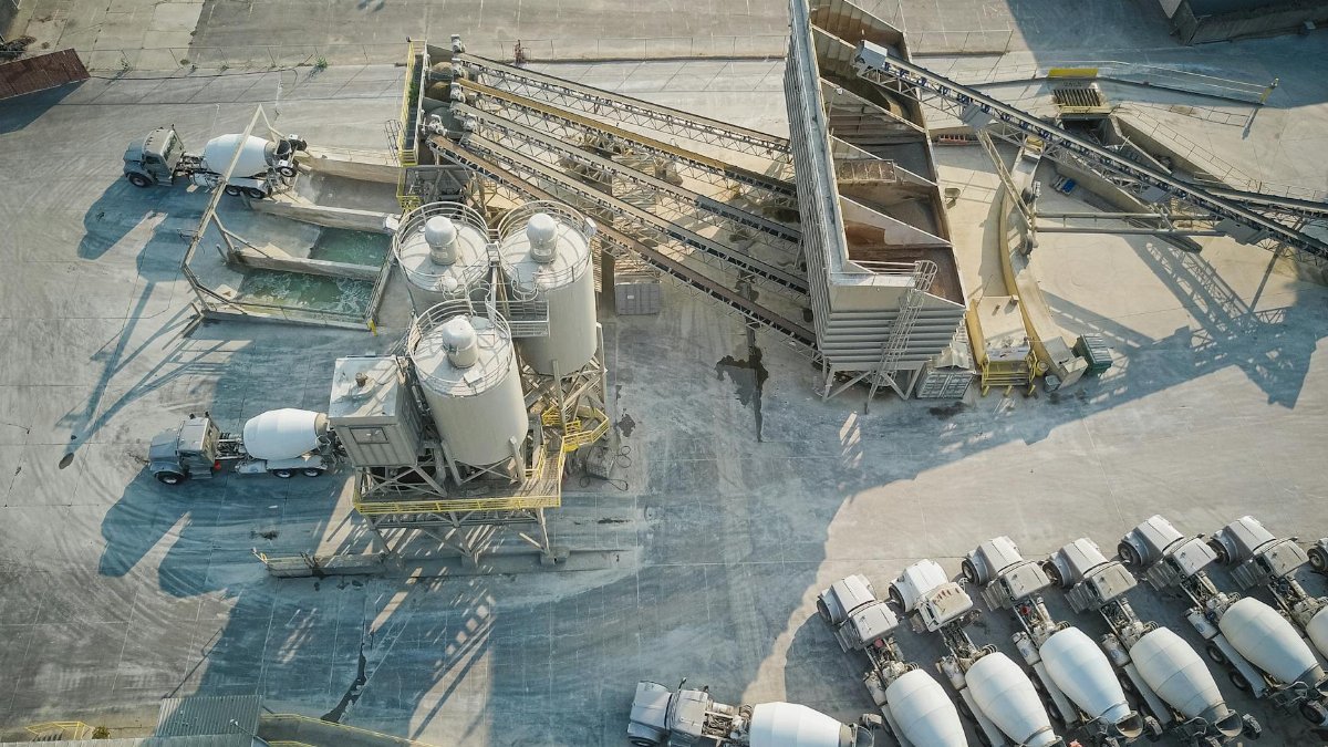 A drone-captured aerial view of an industrial concrete mixing plant with trucks and machinery.