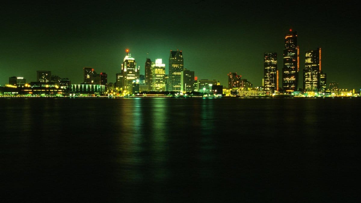 Stunning nighttime view of Detroit's illuminated skyline across a calm river under a dark sky.