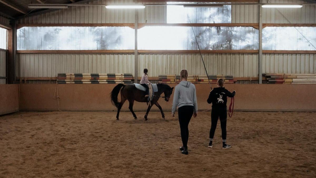 A young girl receives horse riding lessons indoors under guidance.