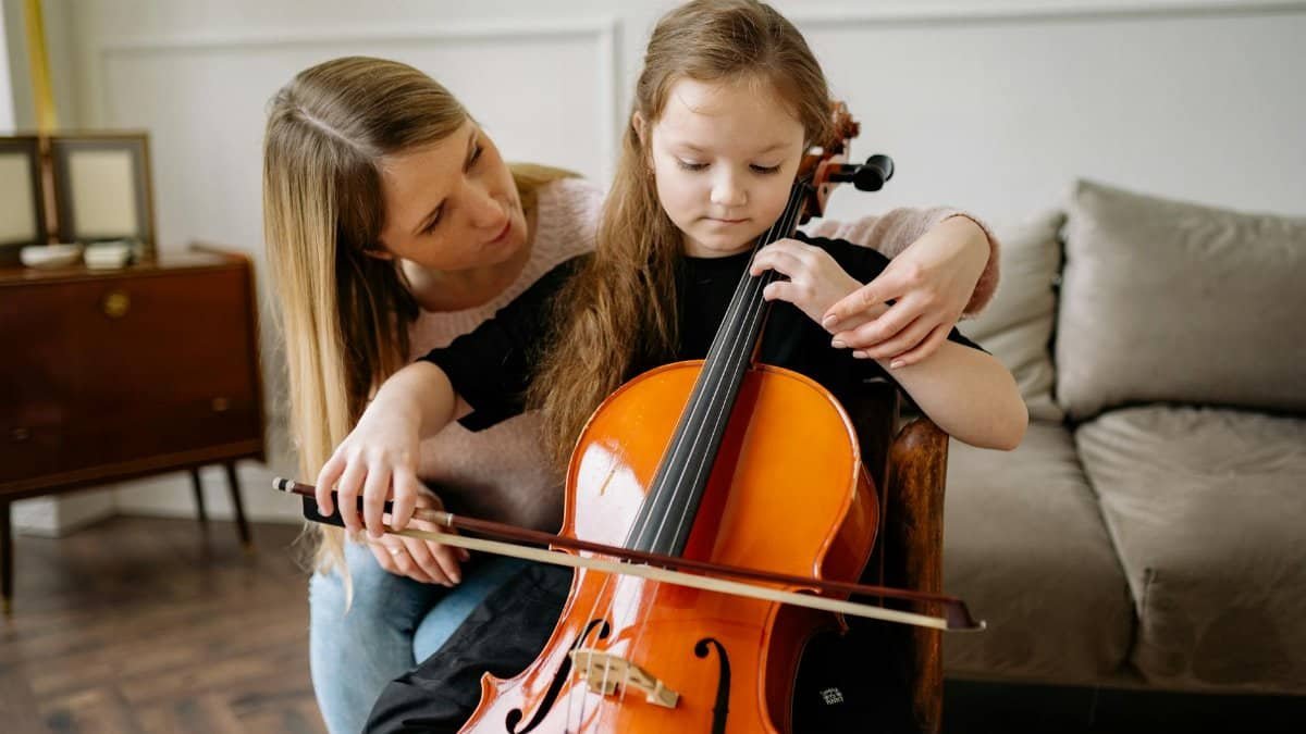A young girl receiving cello lessons from a teacher in a cozy living room setting.