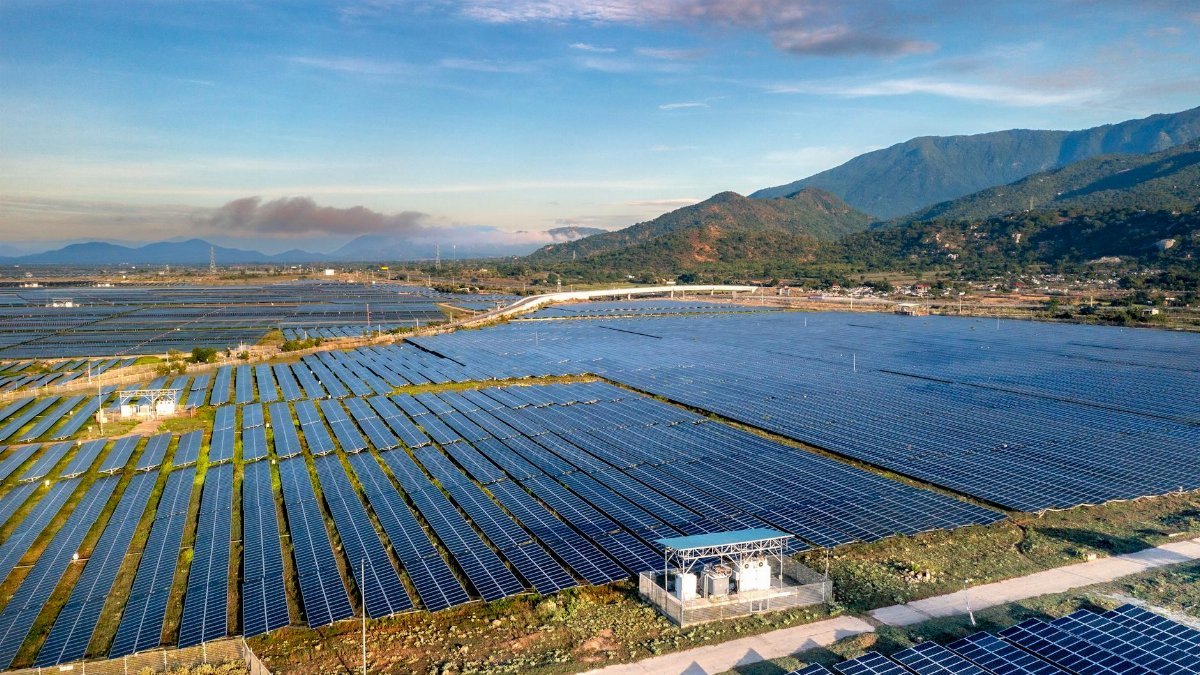 Expansive solar farm with rows of panels in Vietnam, framed by distant mountains under a clear sky.