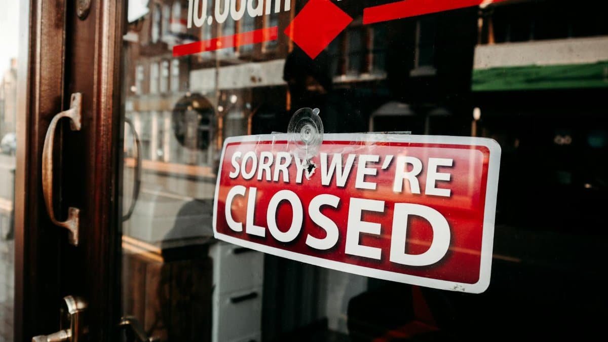 Close-up of a shop's closed sign on a glass door reflecting the street outside.