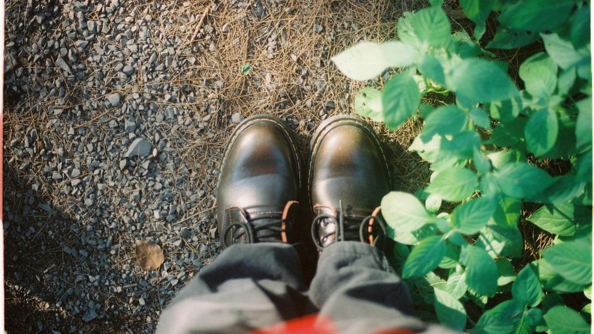 Artistic perspective of sturdy boots on gravel next to vibrant greenery in natural light.