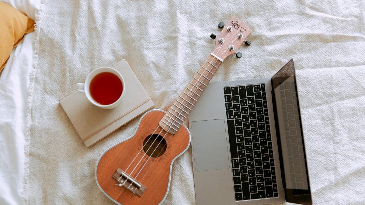 A cozy composition featuring a ukulele, laptop, and cup of tea on a bed for a relaxing indoor ambiance.