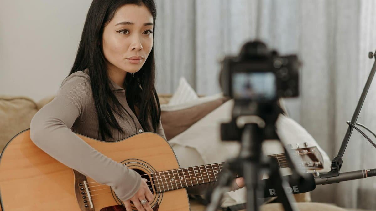 Asian woman playing acoustic guitar during an online music lesson at home.
