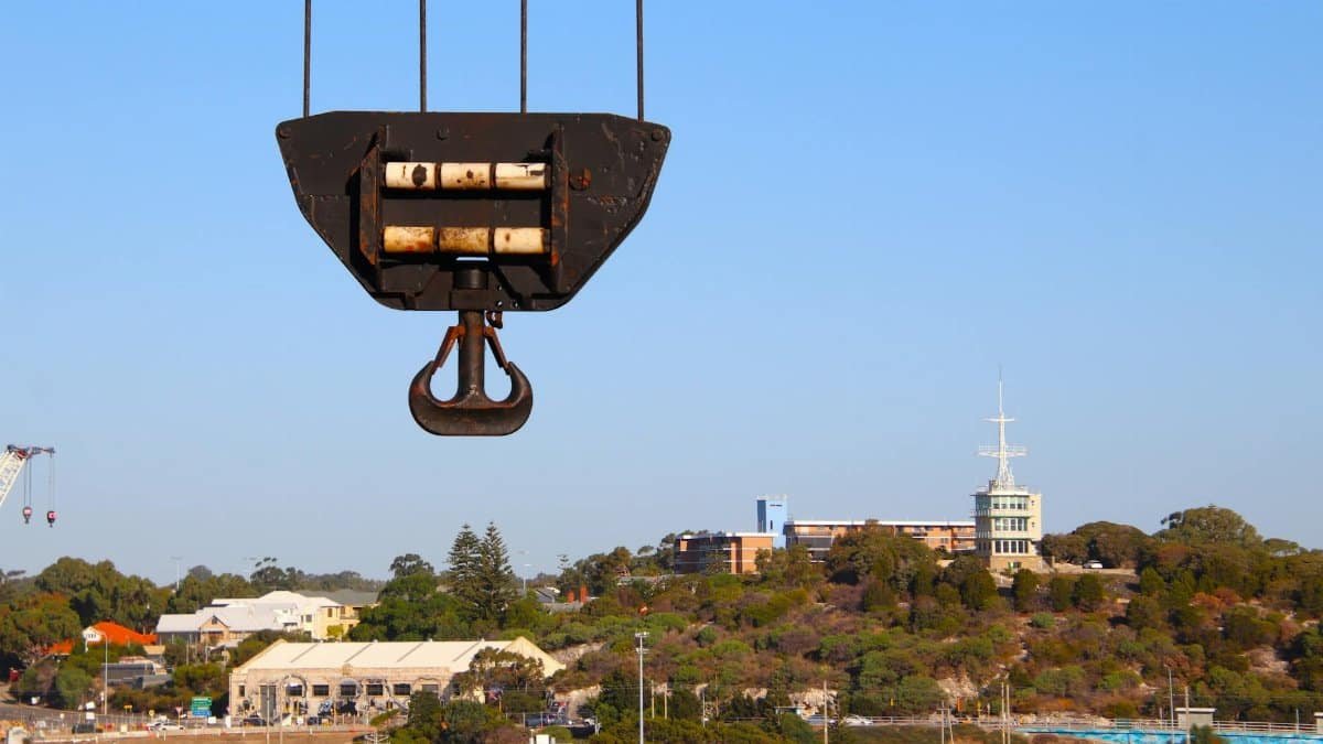 Close-up of a crane hook with a cityscape background, showcasing urban industrial themes.
