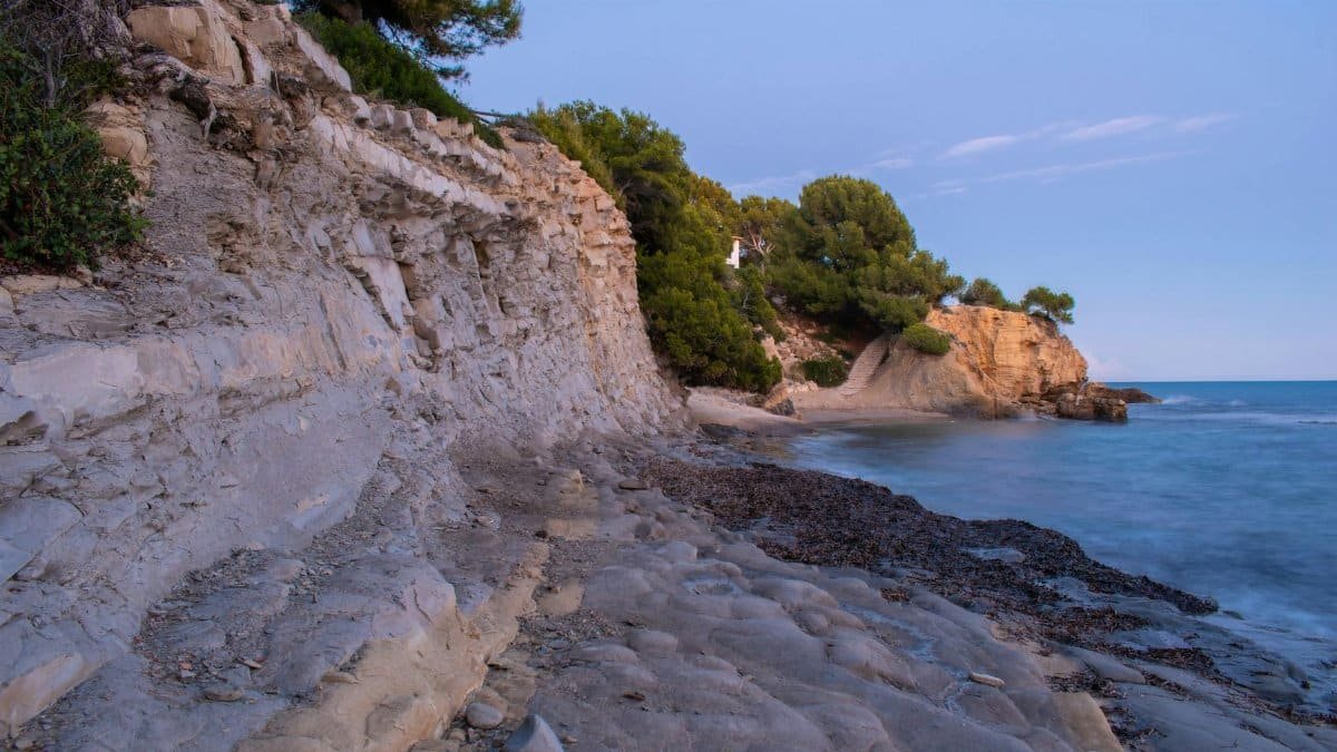 Scenic view of a rocky coastal beach at twilight with calm sea and cliffs.