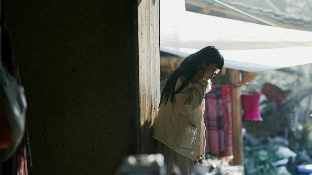A woman stands thoughtfully outside, partially in shadow, capturing a serene moment.