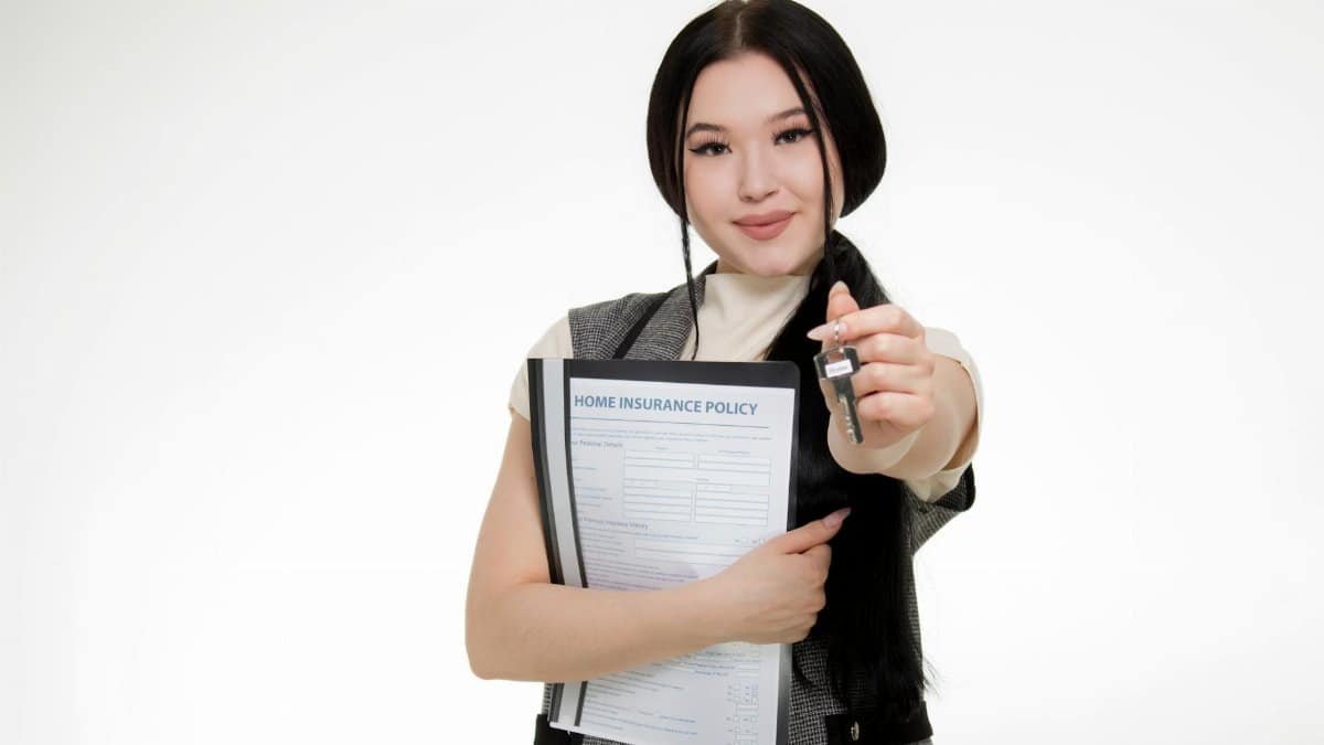 Asian woman smiling while holding a home insurance policy and a key, symbolizing new home ownership.