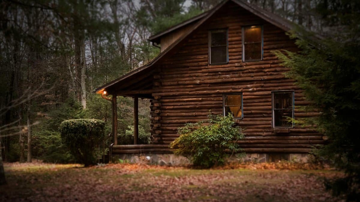 A cozy log cabin surrounded by autumn trees, showcasing warm lighting and tranquil nature.