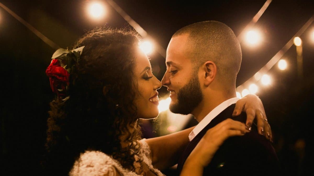 A joyful wedding couple embracing under romantic string lights at night.