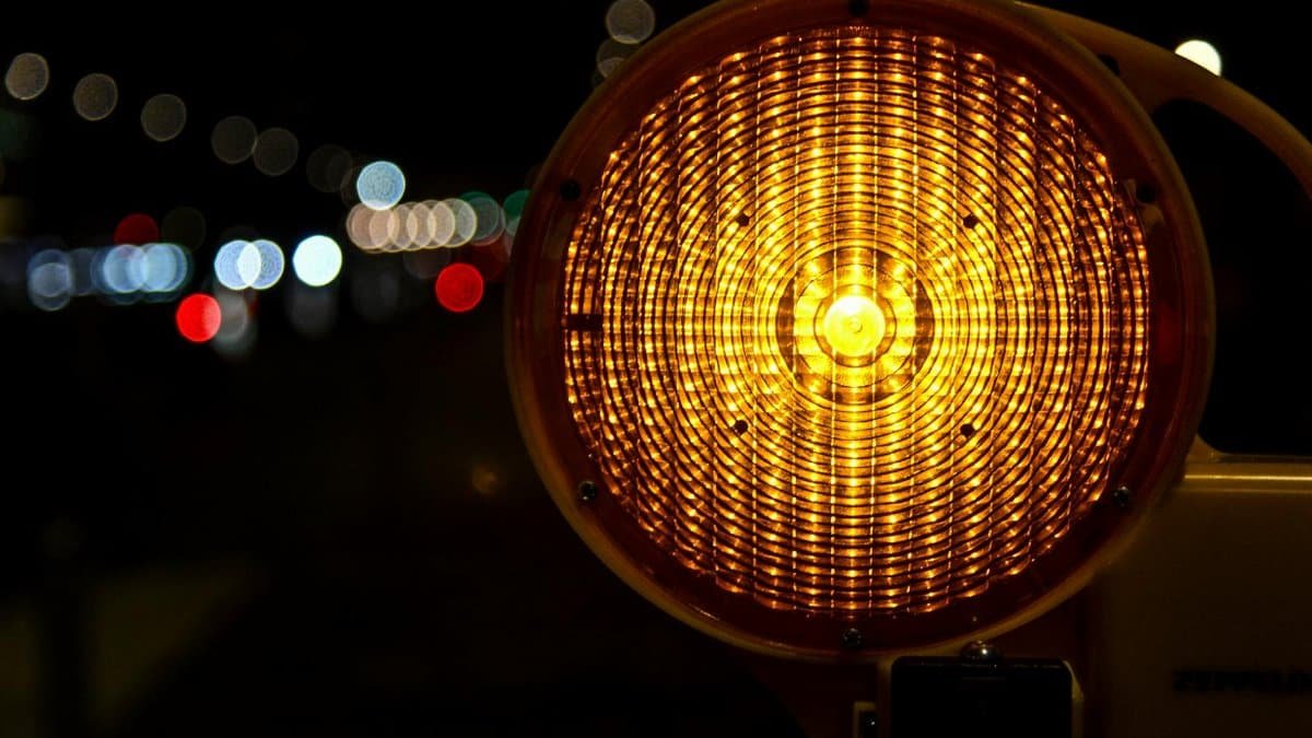 A reflective traffic warning light glowing in the nighttime with bokeh effect.