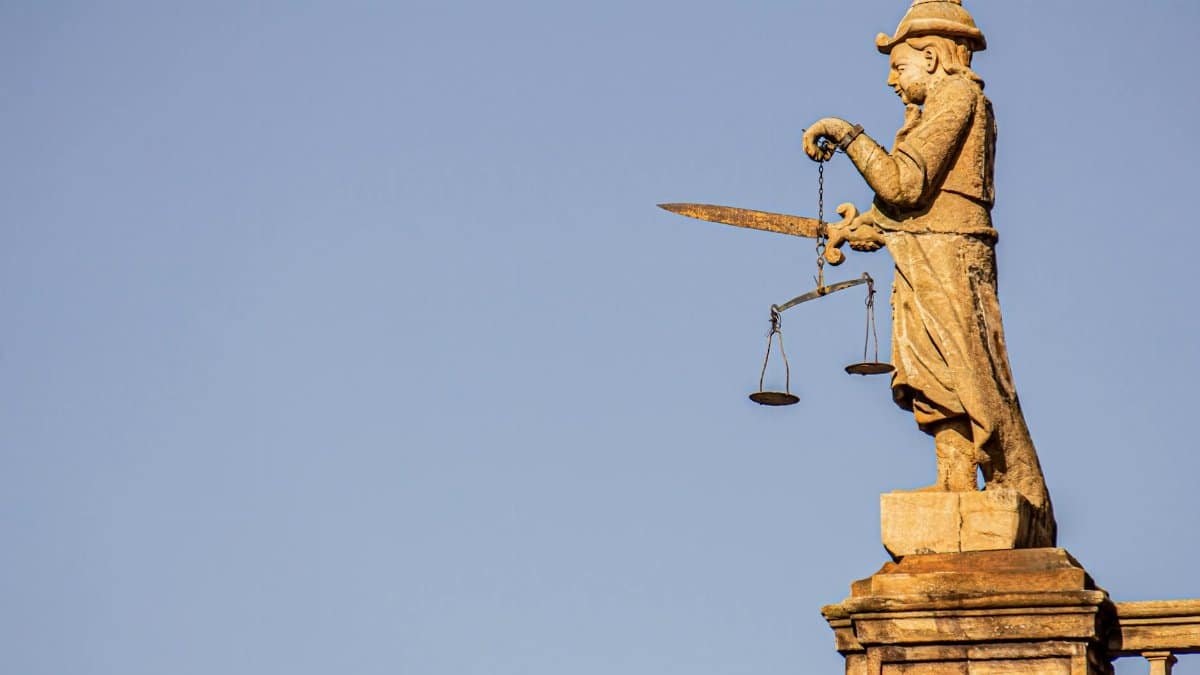A side view of a justice statue with a sword and weighing scales against blue skies.